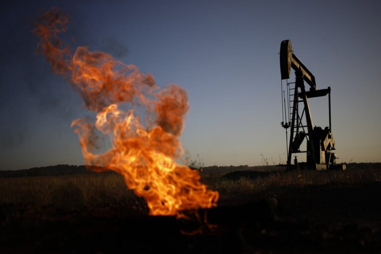 A natural gas flare burns near an oil pump jack